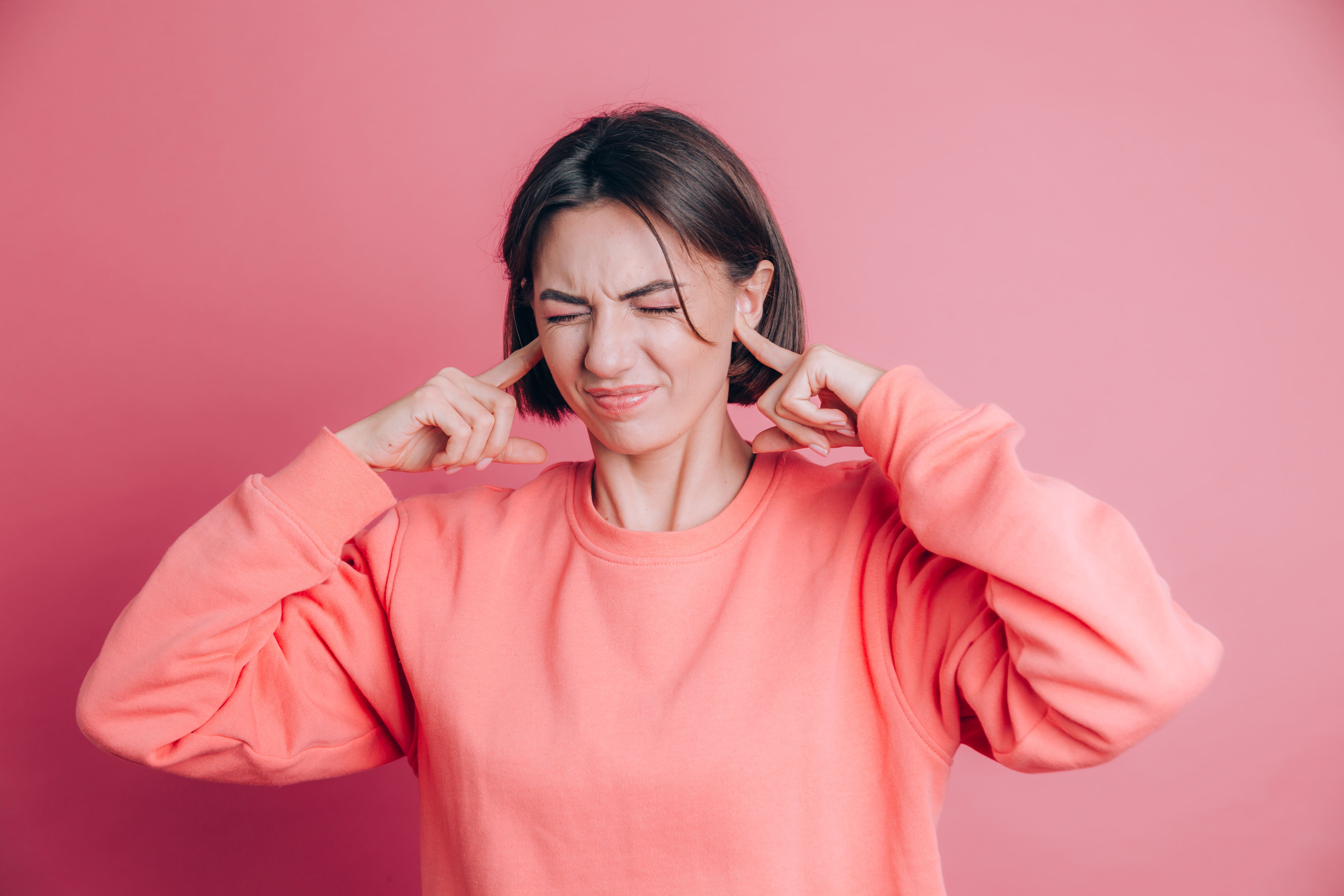 femme portant un pull decontracte sur fond couvrant les oreilles avec les doigts avec une expression agacee pour le bruit de la musique forte 2
